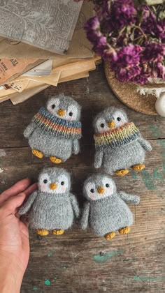 three small knitted owls sitting on top of a wooden table next to purple flowers