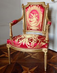 a red and gold chair sitting on top of a wooden floor next to a white door