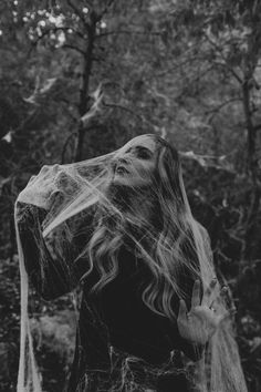 a woman with long hair standing in front of trees covered in spiderwetches