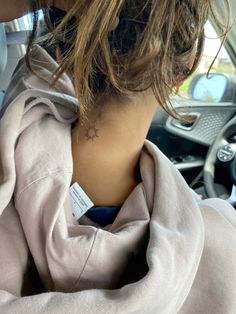 a woman with a small star tattoo on her neck sitting in the drivers seat of a car