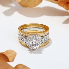 two gold and white wedding bands with a diamond ring in the middle, on top of leaves