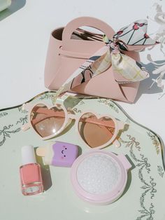 the contents of a purse, sunglasses and nail polish are laid out on a plate