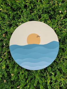 a painted plate sitting in the middle of some grass with an ocean scene on it