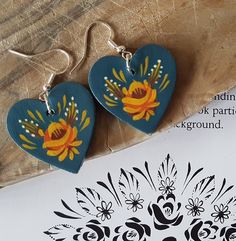 two heart shaped wooden earrings with flowers painted on them sitting next to a piece of paper