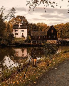 an old house next to a river with a lamp on the side and autumn foliage around it