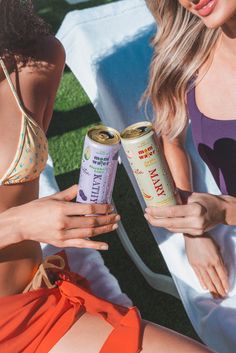 two women in bikinis holding cans of beer