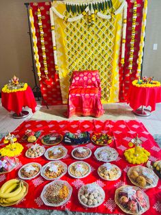 a red table topped with lots of food next to a yellow and red wall covered in decorations