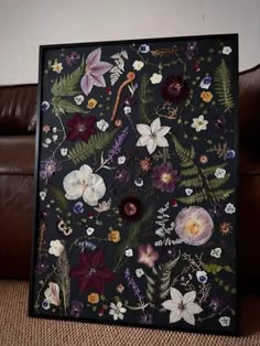 a black frame with flowers and leaves on the front is sitting next to a brown leather couch