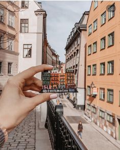 a person holding up a small piece of paper in front of some buildings on a city street