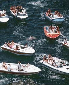 many people are riding on small boats in the water with one man swimming behind them