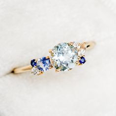 an engagement ring with three different colored stones on it's side, sitting on a white surface