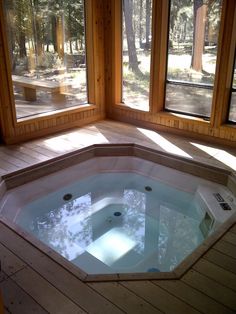 an indoor hot tub in the middle of a wooden floored room with large windows