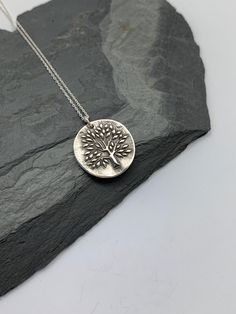 This unique tree of life handmade embossed round pendant has been entirely handmade using .999 fine silver. It has been cut from fine silver precious metal clay, textured, fired and oxidized. The pendant hangs from a sterling silver diamond cut cable chain. This fine silver pendant features an embossed tree of life on one side of the pendant and is reversible to a tiny leaves embossed pattern on the reverse side. Pendant size: approximately 3/4 x 3/4 inches Chain length: adjustable at 16 and 18 Nature-inspired Silver Etched Necklaces, Silver Etched Nature-inspired Necklaces, Silver Round Stamped Necklaces, Sterling Silver Stamped Round Necklace, Sterling Silver Etched Round Disc Necklace, Silver Tree Of Life Round Pendant Necklace, Handmade Silver Round Disc Necklace, Silver Nature-inspired Necklace For Everyday, Silver Handmade Round Disc Necklace