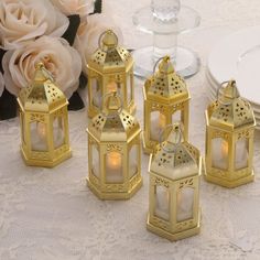 four gold lanterns sitting on top of a table next to white plates and pink flowers