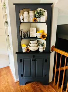 a black china cabinet with sunflowers and dishes on the top, next to a stair case