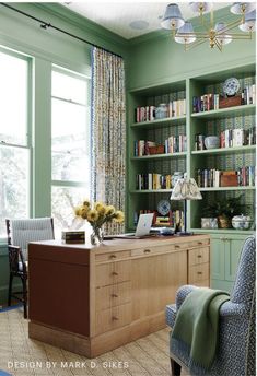 a home office with green walls and blue chairs in front of a book shelf filled with books