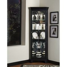 a glass cabinet with wine glasses and plates in front of pictures on the wall behind it