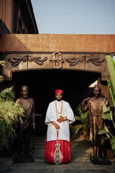 a man standing in front of statues wearing a red and white outfit with an orange hat