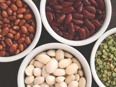 four white bowls filled with different types of beans and pistachios on a table