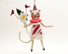 a white cat figurine holding a flower and wearing a red and white dress