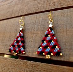 two red, white and blue beaded christmas trees are hanging from hooks on a wooden surface