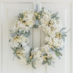 a wreath with white flowers and greenery hangs on a door