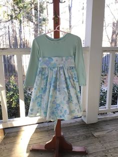 "This adorable girls size 4 Dress has a pastel sage bodice in soft cotton knit and a pastel watercolor skirt in shades of blue, aqua, sage, and white. A wide sash is attached at the side seams and ties into a beautiful bow in the back.  Measurements: 23\" from shoulder to hem, 14\" at waist from side seam to side seam, 12.5\" sleeve from shoulder to wrist hem.  Machine wash warm and tumble dry low heat, or line dry. Touch up with medium heat iron.  All Carolina Wren Original items are created and sewn in my smoke free sewing studio in Apex, NC.  My cat rules my home but she doesn't sew and doesn't have access to my fabric. ❤️" Light Blue Long Sleeve Cotton Dress, Fitted Light Blue Cotton Dress, Fitted Spring Dress, Spring Flowy Dress With Gathered Skirt, Cotton Long Sleeve Fitted Dress, Cotton Long Sleeve Dress With Fitted Bodice, Long Sleeve Cotton Dress With Fitted Bodice, Blue Cotton Dress With Gathered Skirt, Fitted Long Sleeve Dress With Gathered Skirt