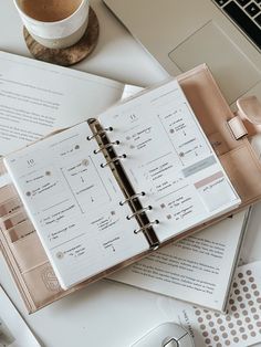 an open planner sitting on top of a desk next to a cup of coffee and a laptop