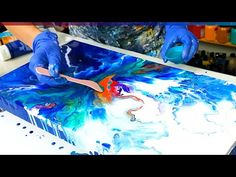 a person in blue gloves is painting on a large piece of paper with acrylic paint