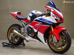 a red, white and blue motorcycle parked in front of a gray wall with the words honda on it