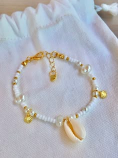 This bracelet features luminous white beads, reminiscent of sea shells and ocean foam, paired with gold beads, and pearls to evoke the warmth of the sand. It also has little gold shell charms for that perfect jangle sound like shells in a bowl. This beachy vibe is perfect for summer and any outfit :) Seashell Bracelet Ideas, Sea Shells Bracelet, Seed Bead Bracelet With Charm, Shell Bracelet Ideas, Sea Bead Bracelets, Shell Bracelet Diy, Beaded Bracelets Summer, Summer Bracelet Ideas, Summer Beaded Bracelets