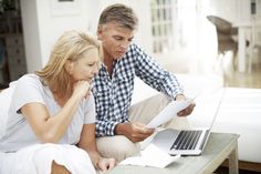 a man and woman sitting on a couch looking at papers in front of a laptop