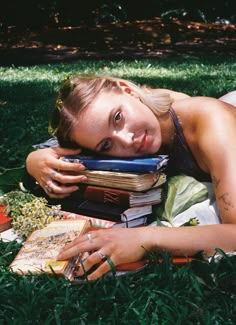 a woman laying on the grass with books in her hands and looking at the camera