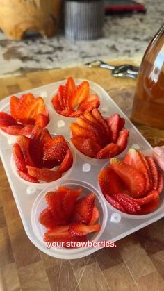 some strawberries are placed in cups on a table next to a bottle of honey