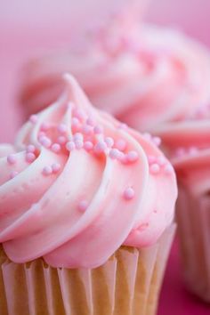 three cupcakes with pink frosting and sprinkles on them are sitting next to each other