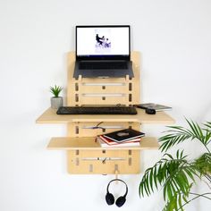 a laptop computer sitting on top of a wooden shelf next to a potted plant