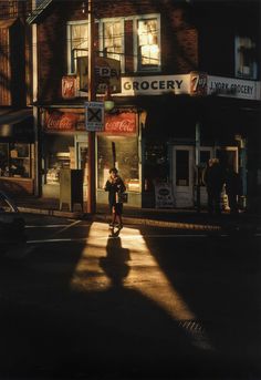 a person walking down the street in front of a grocery store at night with long shadows on the ground