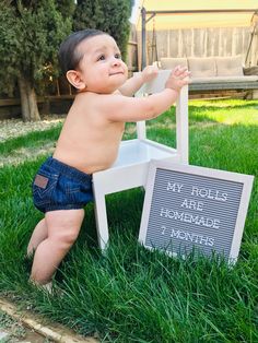 a baby sitting on top of a chair in the grass next to a chalkboard