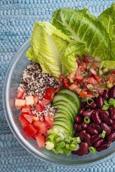 a salad with lettuce, tomatoes, beans and avocado in a glass bowl