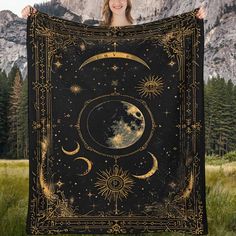 a woman holding up a black and gold tapestry with the moon and stars on it