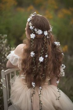 a woman with long hair sitting on a chair wearing a dress and flowers in her hair