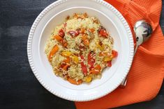 a white bowl filled with rice and vegetables on top of an orange napkin next to a fork