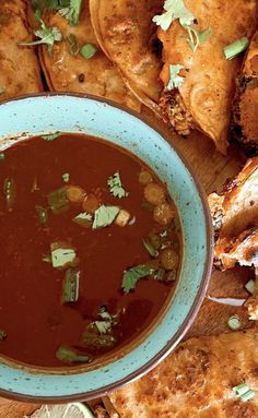 a bowl of soup next to some fried food on a cutting board with lemon wedges