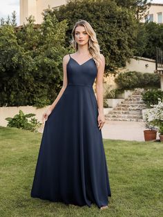 a woman standing in the grass wearing a long blue bridesmaid dress with spaghetti straps