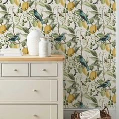 a white dresser sitting next to a wall covered in yellow and green fruity wallpaper