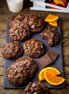 chocolate cookies and oranges are on a slate tray with milk in front of them