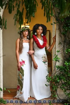 two women in white dresses standing next to each other with flowers on their heads and leis around their necks