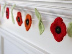 red and green felt poppys are hung on a white fireplace mantel with leaves