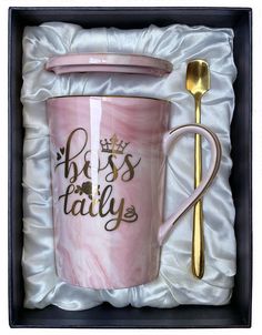 a pink and gold coffee cup with a spoon in it, sitting inside a box