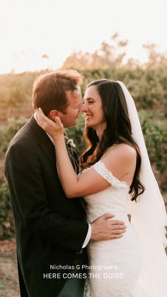 a bride and groom standing close to each other in front of some bushes at sunset